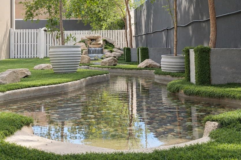 The Little Gems outdoor park: trees, turf and a shallow pebble pond with a small waterfall